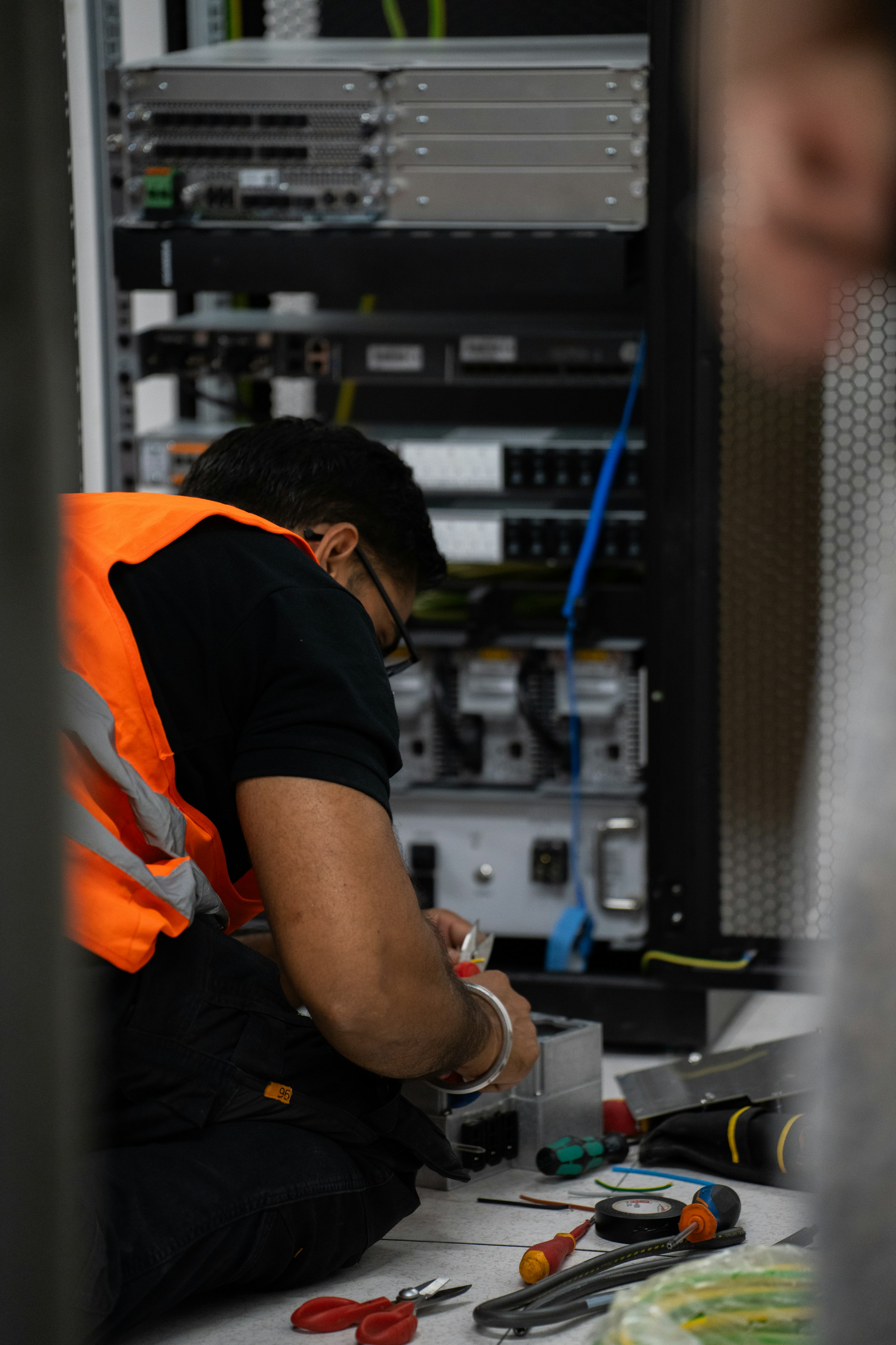 A Trahezy technician in a hi-vis vest wiring a network rack, focused on the work